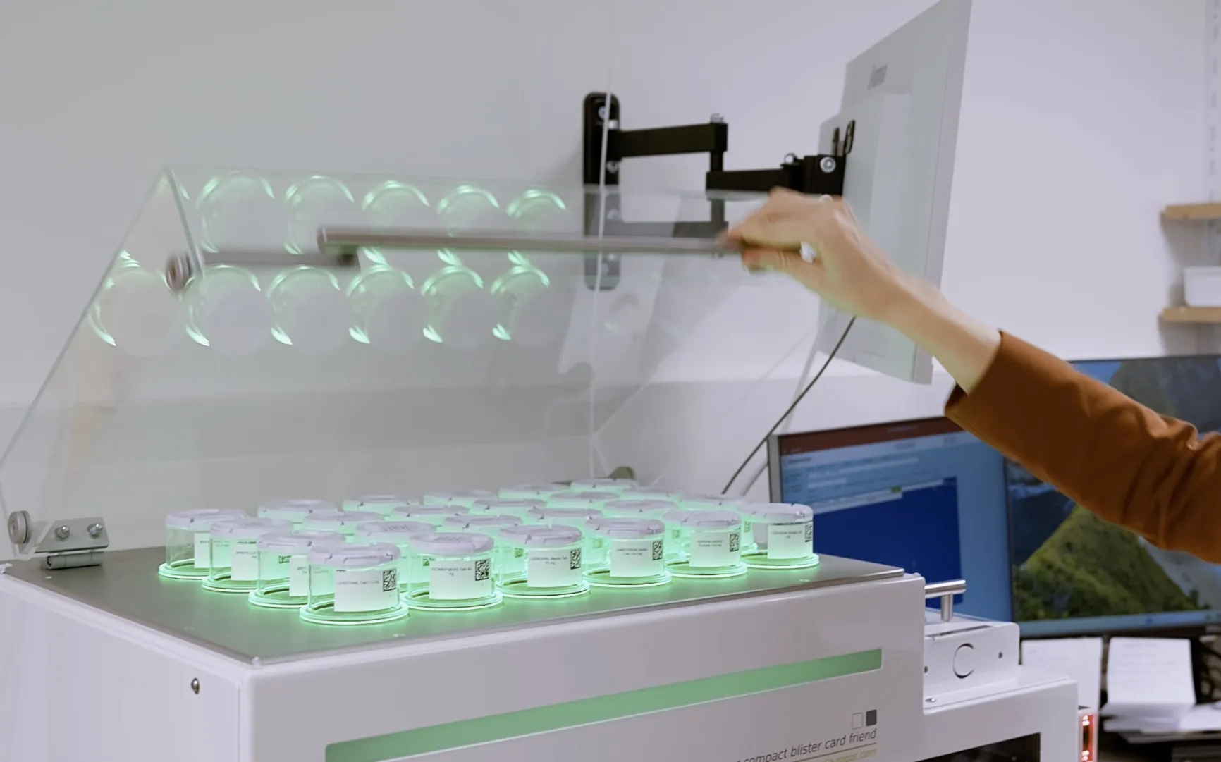 A hand at the open blister machine with weekly doses lit in green