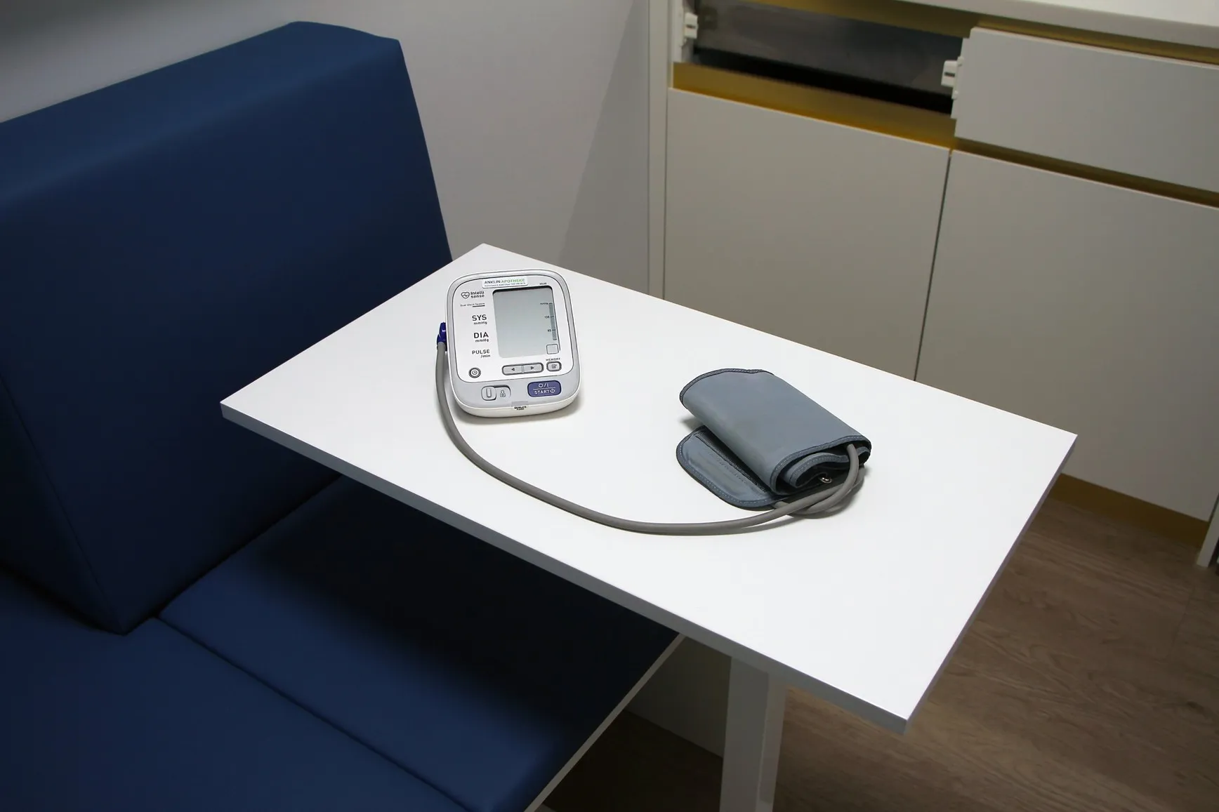 An upper-arm blood pressure monitor with cuff on a table in the consulting room