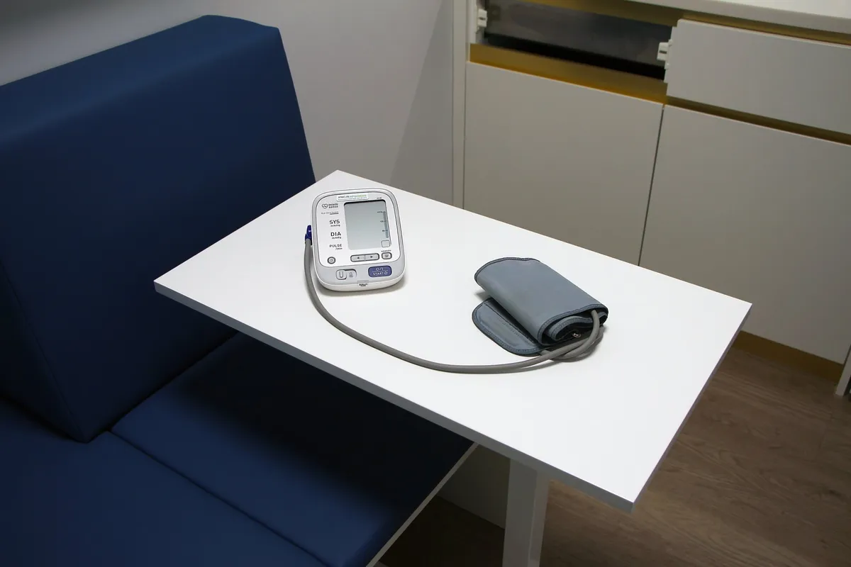 An upper-arm blood pressure monitor with cuff on a table in the consulting room