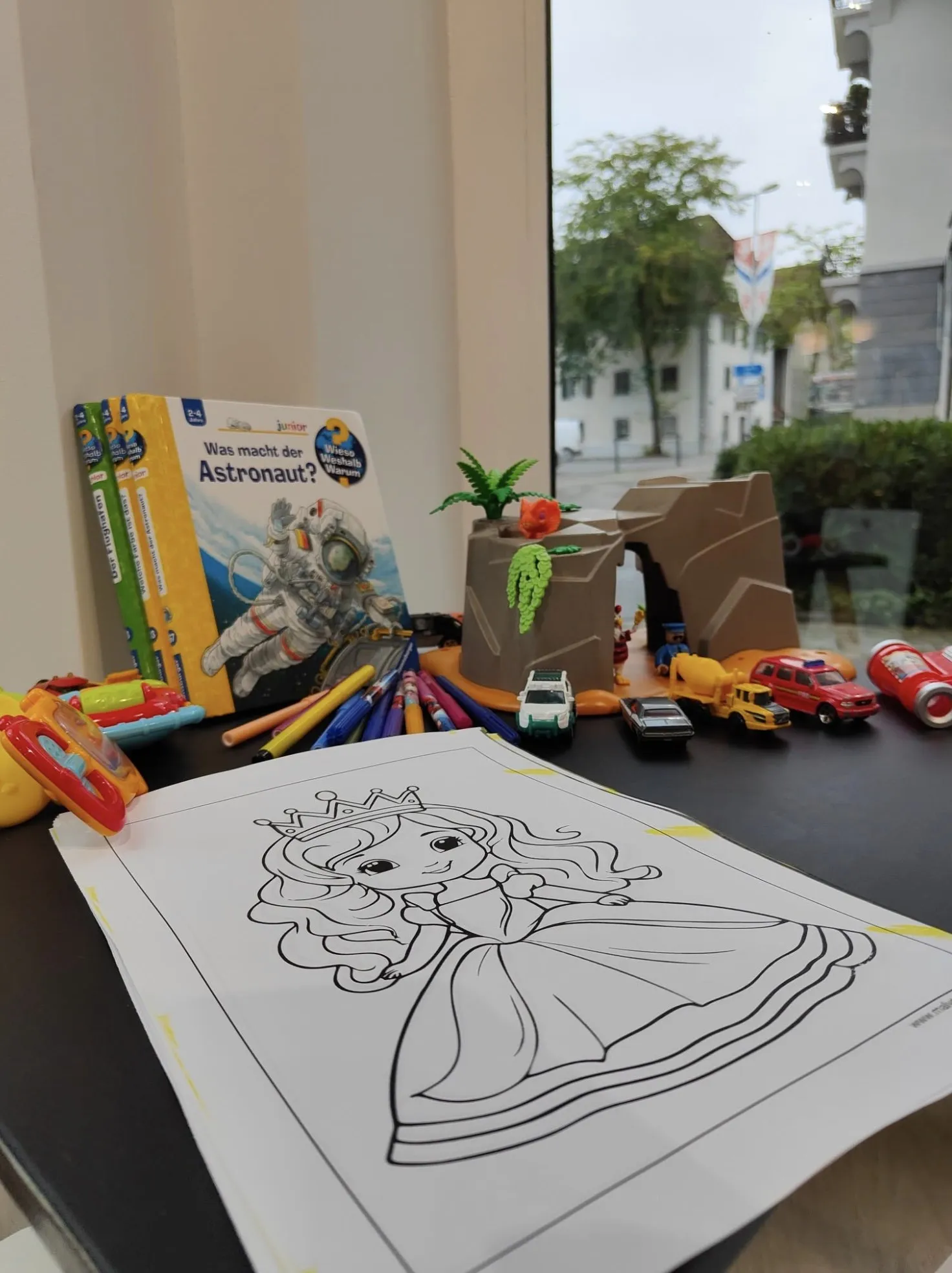 The play corner of Anklin Apotheke with picture books, a colouring sheet and toys by the window