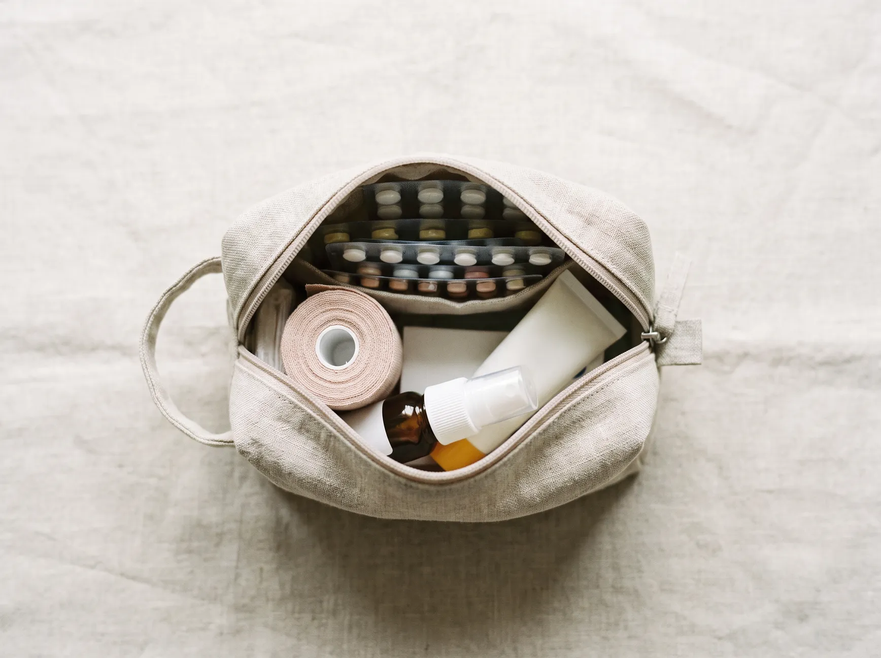 An open wash bag with plasters, gauze and a small tube, seen from above