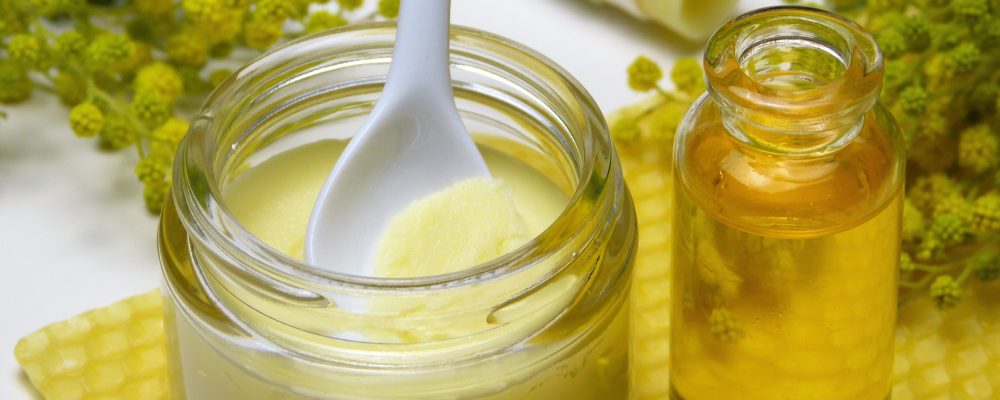 Naturkosmetik: Cremetiegel und Ölflasche auf Honigwaben, Kamille und Lippenpomade im Hintergrund